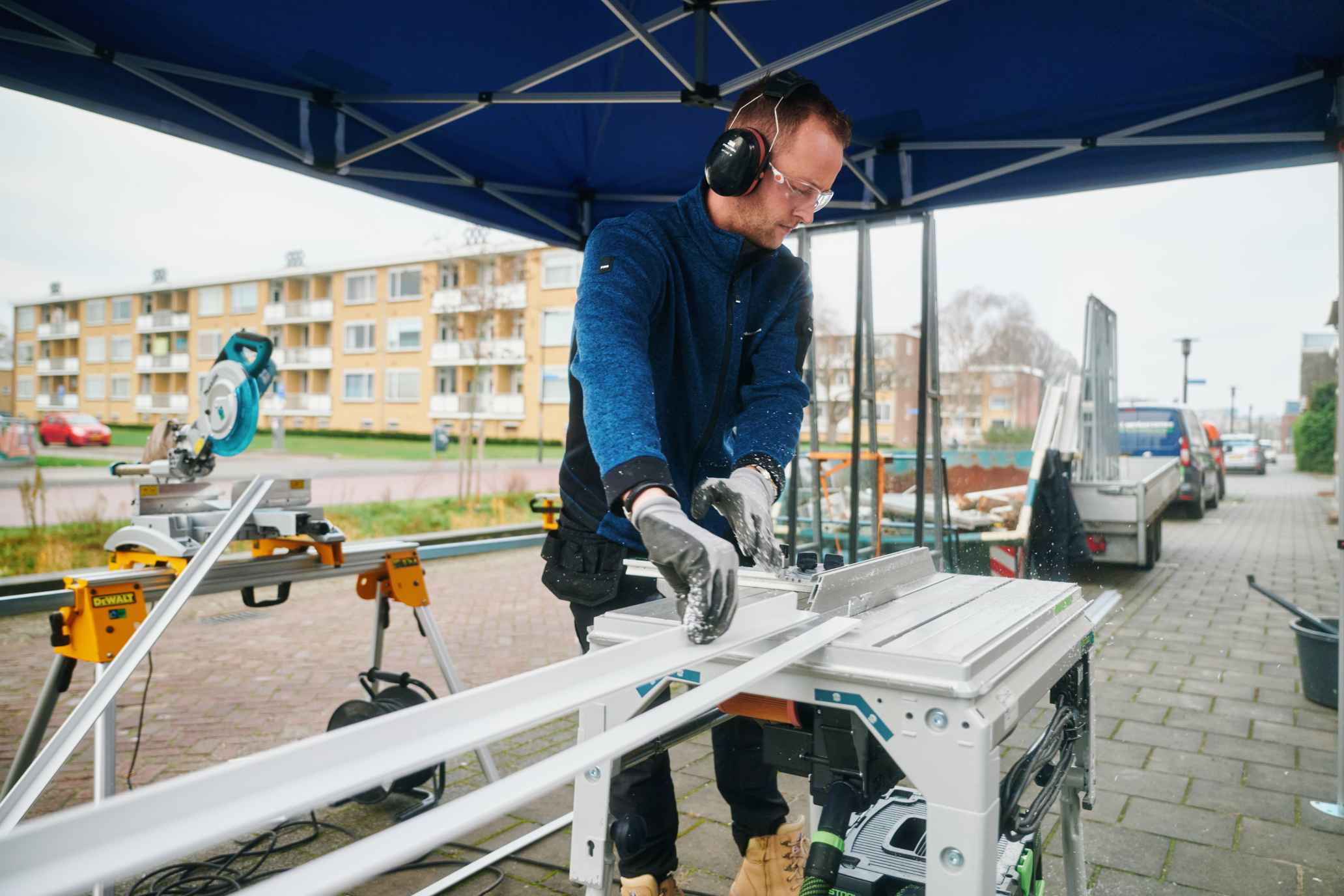 Monteur zaagt kunststof profielen op locatie, met appartementengebouwen op de achtergrond