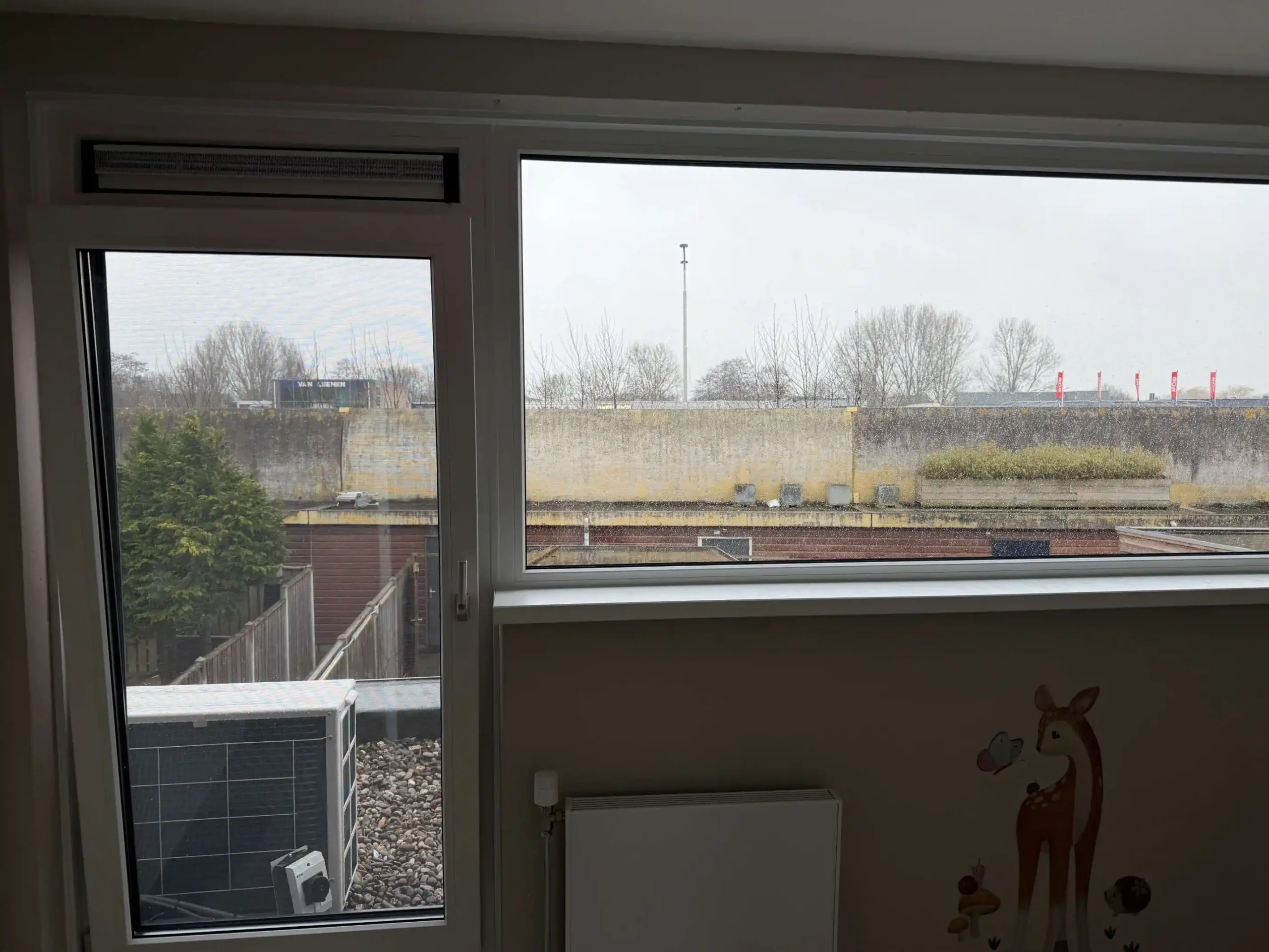 Wit kunststof kozijn in een kinderkamer met een ventilatierooster bovenin het draaiende raam