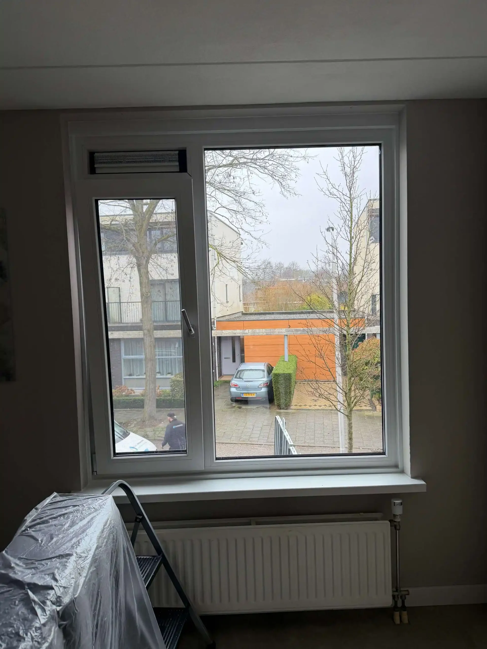 Nieuw wit kunststof kozijn in een woonkamer, met meubels afgedekt met folie tijdens de werkzaamheden
