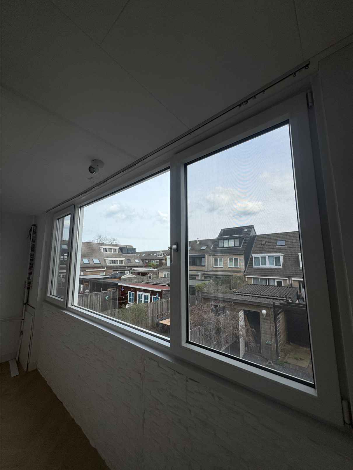Nieuw wit kunststof kozijn van binnenuit gezien met uitzicht op de achtertuinen
